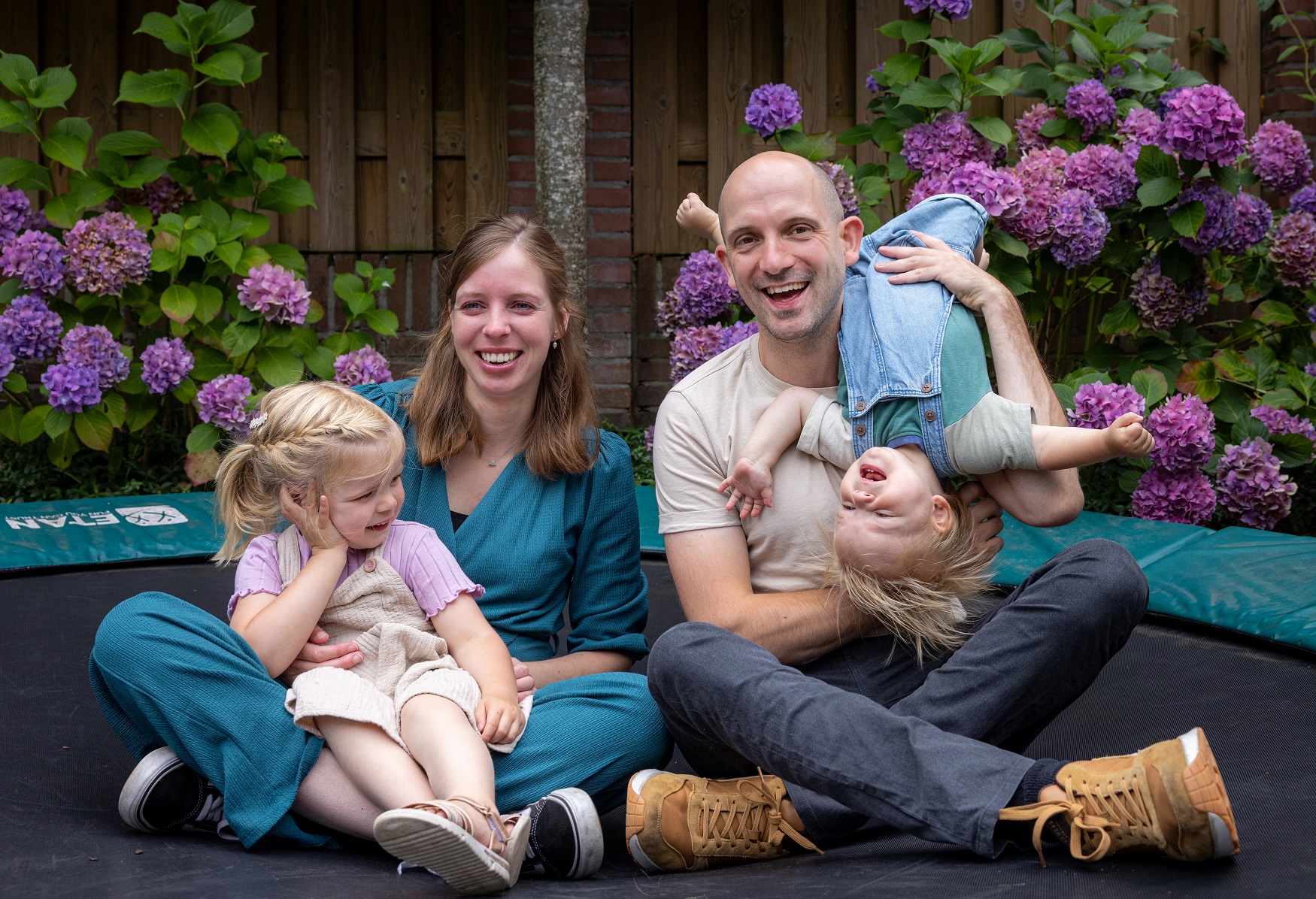 Man en vrouw zitten met hun 2 kinderen op de trampoline