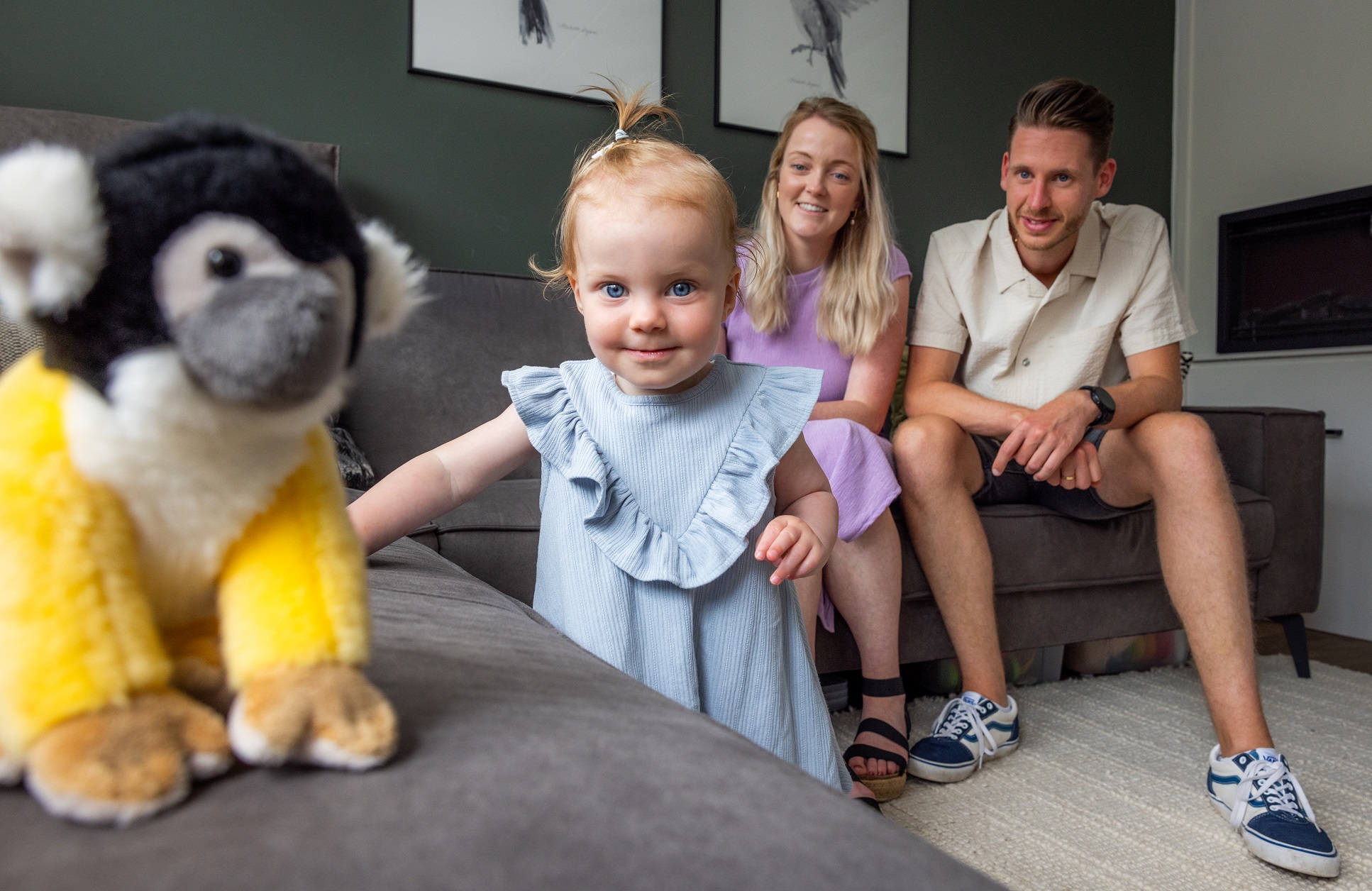 Man en vrouw op zitbank en hun dochter op de voorgrond met een knuffel